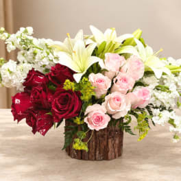 Bouquet of red and pink roses with white lilies in a rustic wood vase