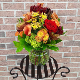 Mixed bouquet of red, orange, and yellow flowers in a clear glass vase