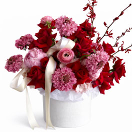 Red and pink flower arrangement in a white hat box with ribbon