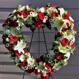 Heart-shaped floral wreath with red roses and white lilies on an easel