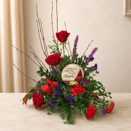 Red roses and purple flowers arranged around a memorial stone on a table