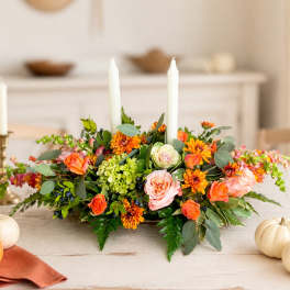 Low floral centerpiece with orange and pink blooms around white taper candles