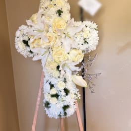 White floral cross arrangement with roses, lilies, and chrysanthemums on an easel