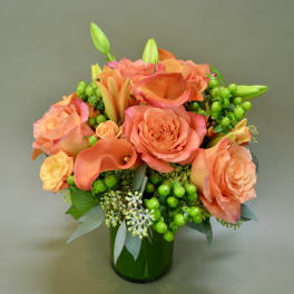 Orange roses and calla lilies in a green glass vase