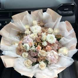 Bouquet of cream and blush roses with pale pink flowers wrapped in white paper
