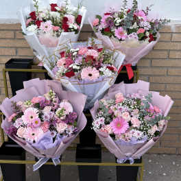 Five pastel flower bouquets arranged on a cart against a brick wall