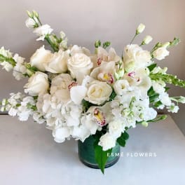 White floral arrangement in a green vase with roses and orchids