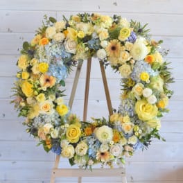 Large floral wreath of yellow, white, and blue flowers on a wooden stand