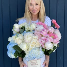 Woman holding a large hatbox arrangement of pink, white, and blue flowers