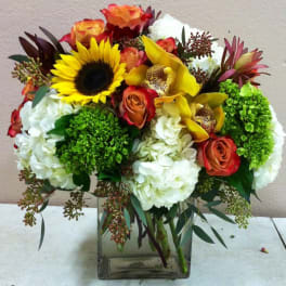 Mixed bouquet with sunflowers, roses, orchids, and white hydrangeas in a glass vase