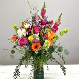 Colorful mixed bouquet in a glass vase with roses, lilies, and gerbera daisies