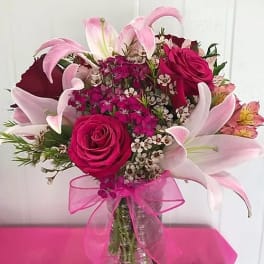 Pink roses and lilies arranged in a glass vase with a pink ribbon