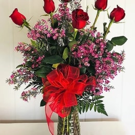 Red roses and pink filler flowers in a glass vase with a red bow