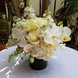 White floral arrangement in a dark vase with orchids and roses