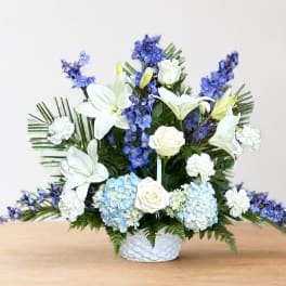 White lilies, roses, hydrangeas, and blue flowers in a white basket