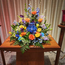 Colorful floral arrangement around a blue urn on a wooden table