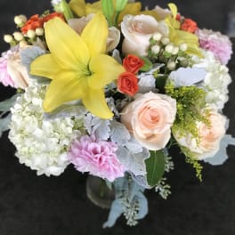 Mixed arrangement with yellow lily, peach roses, white hydrangeas, and pink blooms in a glass vase