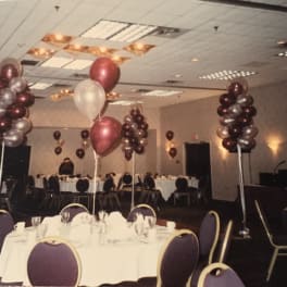 Balloon centerpieces in a banquet hall with round tables and purple chairs