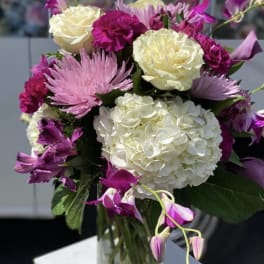 Bouquet of white hydrangeas, pink chrysanthemums, and purple orchids in a glass vase