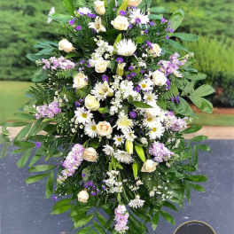 Tall standing spray of white and cream flowers with purple accents on an easel stand