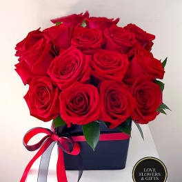 Tight cluster of red roses arranged in a black box with red and black ribbon bow.