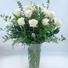 White roses arranged in a clear glass vase with greenery