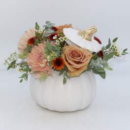 Floral arrangement in a white pumpkin container with peach and orange blooms