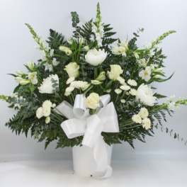 White floral arrangement in a white vase with a large ribbon bow