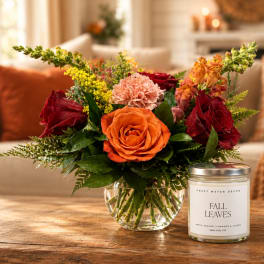 Mixed bouquet of roses and carnations in a glass vase beside a fall-scented candle