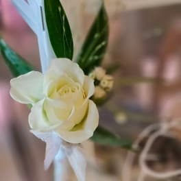 White rose boutonniere with green leaves and a white ribbon