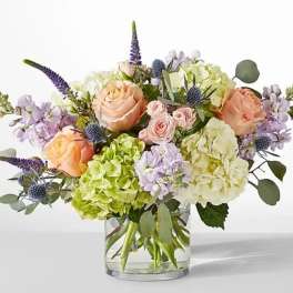 Bouquet of peach roses, hydrangeas, and purple flowers in a glass vase