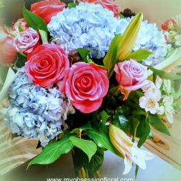 Bouquet of pink roses, blue hydrangeas, and white lilies in a glass vase