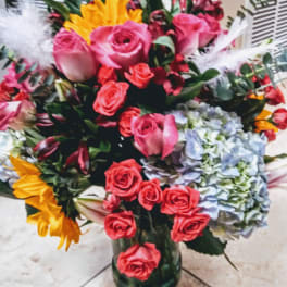 Bouquet of pink and red roses with sunflowers and hydrangeas in a glass vase