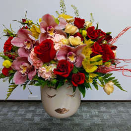 Mixed bouquet of red roses, pink orchids, and yellow flowers in a face vase