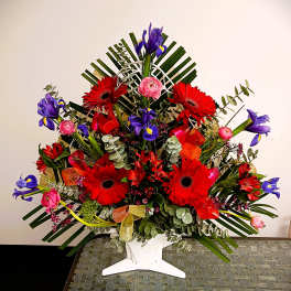 Large floral arrangement with red gerberas, purple irises, and pink blooms in a white vase
