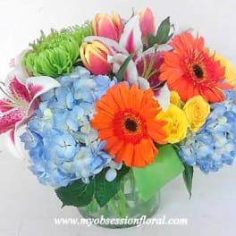 Bright mixed bouquet with blue hydrangeas, orange gerberas, yellow roses and lilies in a glass vase