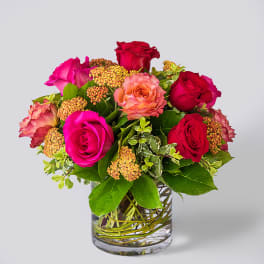 Bouquet of pink and red roses with orange blooms in a clear glass cylinder vase