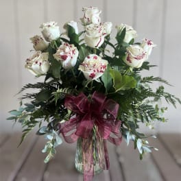 White roses with red speckles in a glass vase with a burgundy ribbon