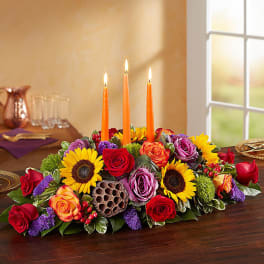 Low floral centerpiece with lit orange candles and mixed roses and sunflowers
