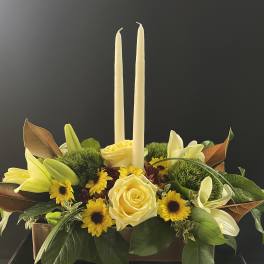 Yellow roses and lilies arranged with two tall candles in a rectangular container
