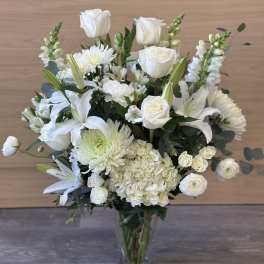 White floral arrangement in a clear glass vase with roses and lilies