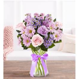 Pink and lavender bouquet in a clear glass vase with a purple ribbon