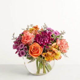 Mixed bouquet of orange, pink, and purple flowers in a clear glass vase