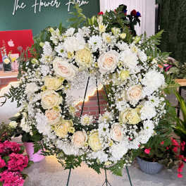 Large white floral wreath on a stand with cream roses and daisies