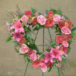 Heart-shaped floral wreath with pink roses and lilies on a stand
