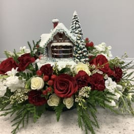 Christmas floral arrangement with red and white roses around a snowy house centerpiece