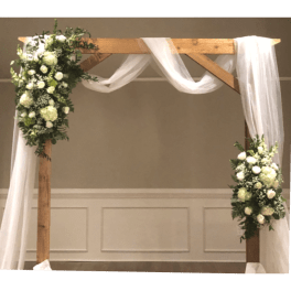 White floral arrangements on a wooden wedding arch with sheer draping