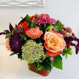 Mixed bouquet with peach rose, coral carnation, and purple blooms in a vase