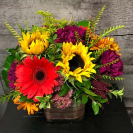 Bright mixed arrangement with sunflowers and red gerbera daisies in a rustic square container