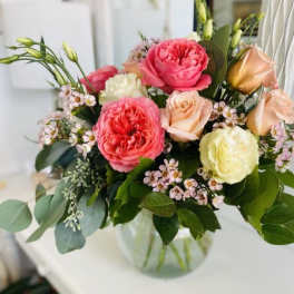 Mixed arrangement of pink and cream roses with small white blossoms in a clear glass bowl vase